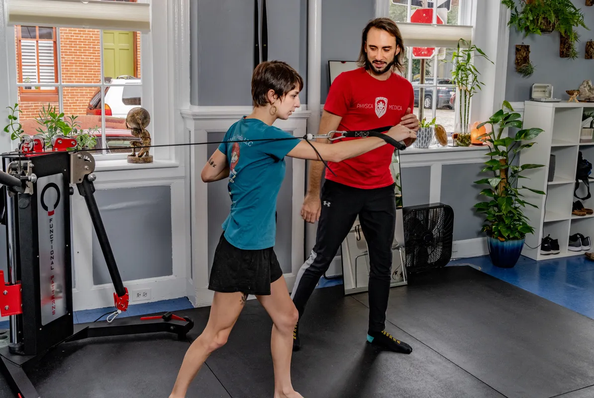 Practitioner in red branded shirt guiding a young client through a functional movement exercise in a modern clinic space.