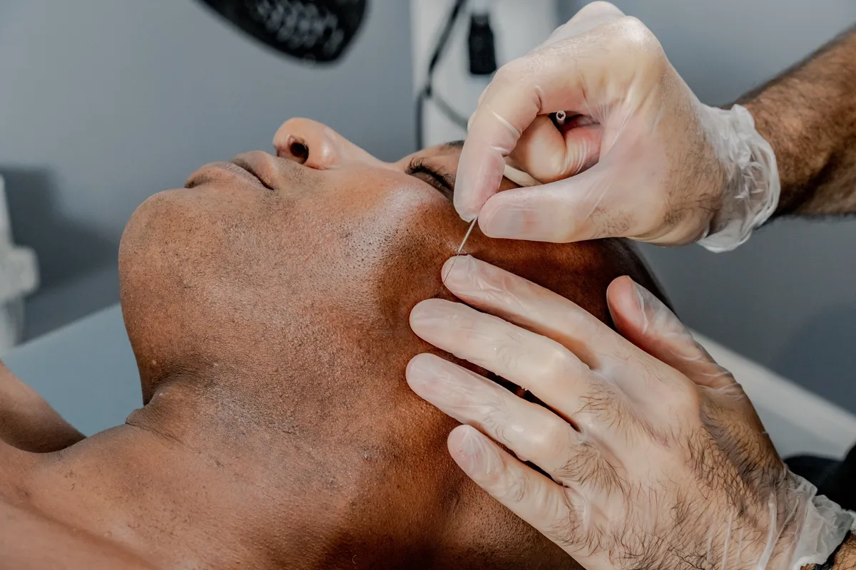 Close-up of hands performing buccal massage or jaw therapy on a client's face and jaw area.