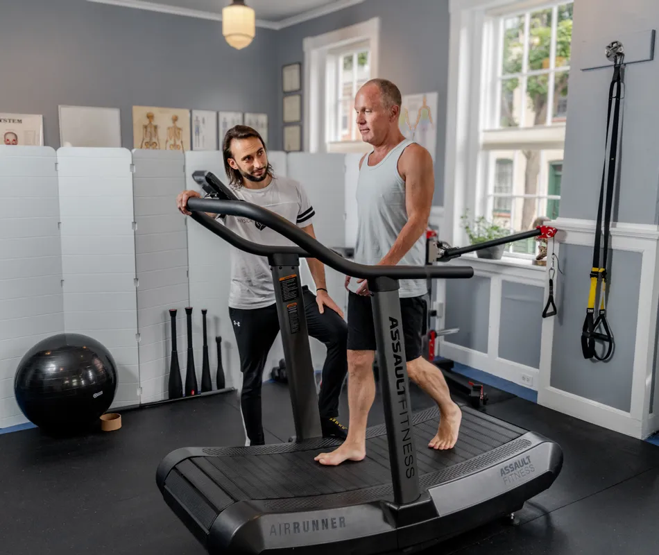 A practitioner instructs a client on proper form while using an exercise bike in a bright, modern therapy room.