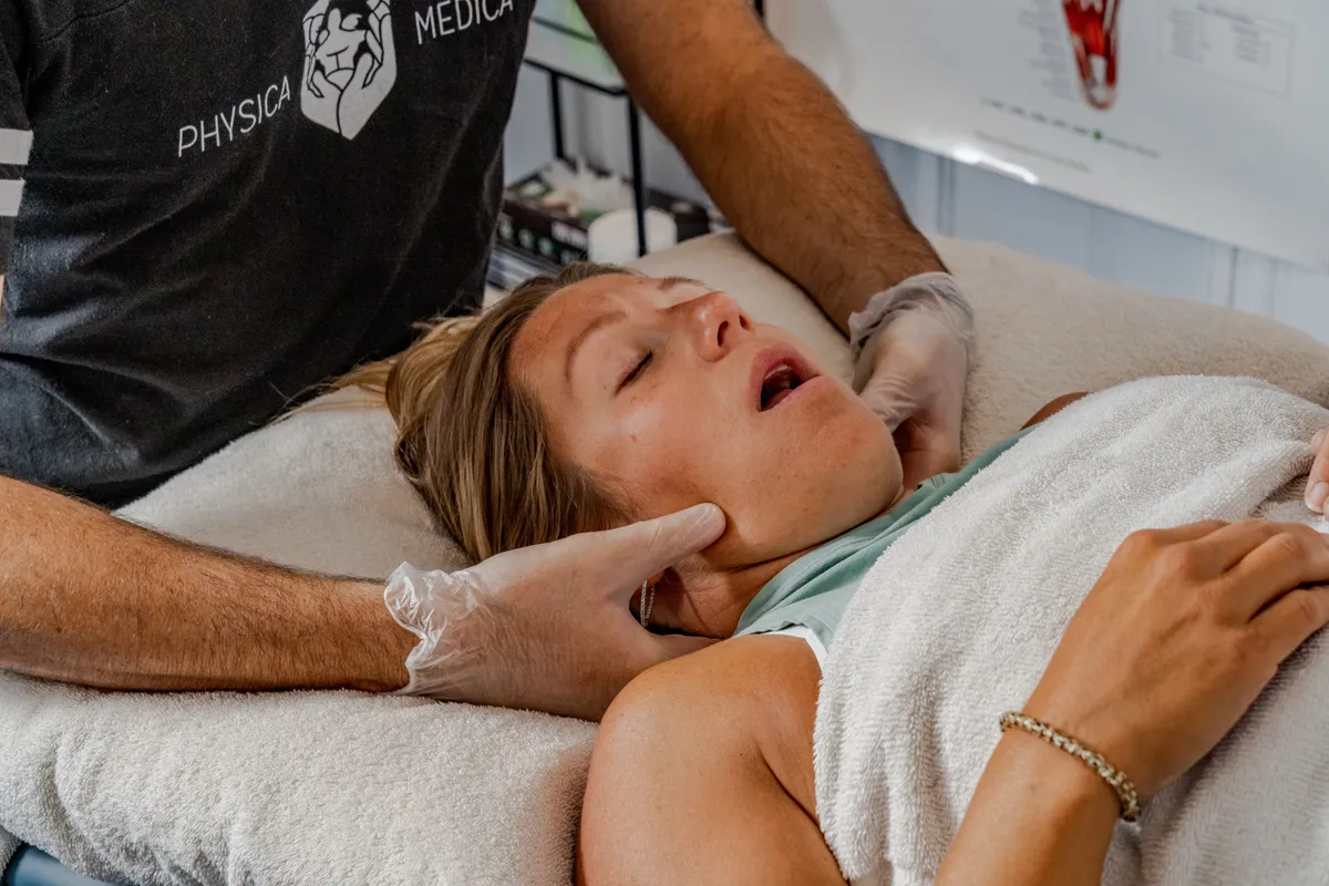 Practitioner performing manual therapy on a client's neck and jaw area while client lies on treatment table