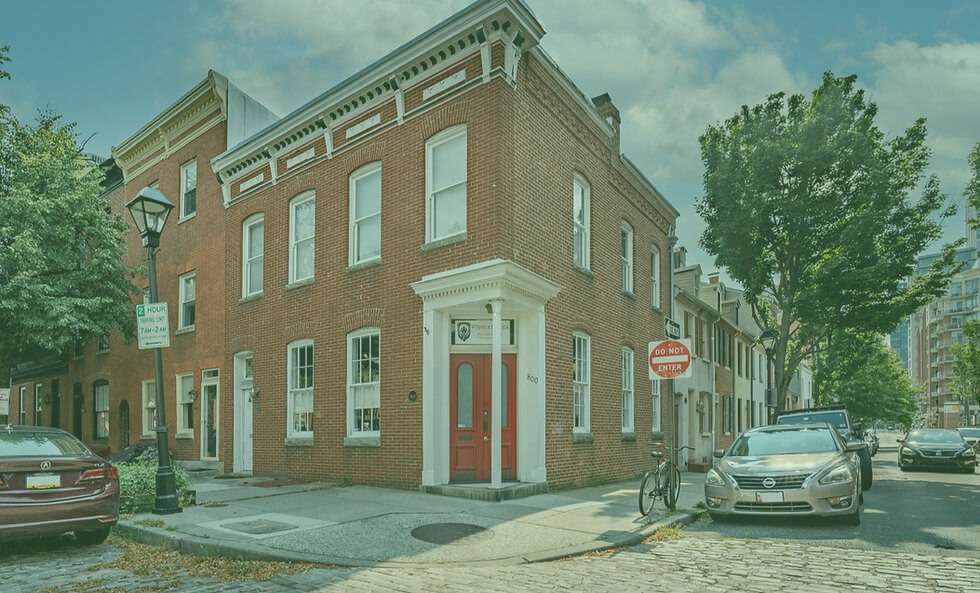 Brick building exterior with red door and white trim on a tree-lined street